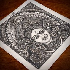 an intricately designed piece of art on a wooden table with a pen and ink