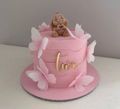 a pink cake decorated with butterflies and a teddy bear sitting on it's top