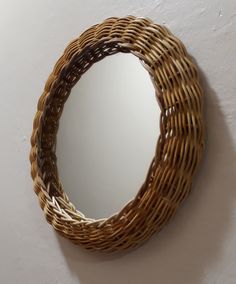 a round mirror hanging on the wall next to a white wall with a wicker frame