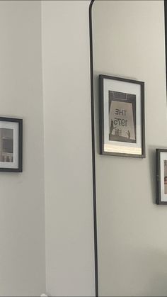 three framed photographs hang on the wall next to a mirror and toilet paper dispenser