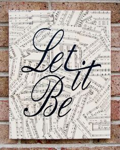 a sign that says let it be on top of a brick wall with sheet music