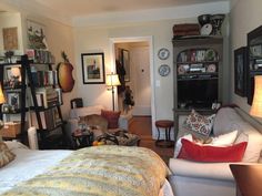 a living room filled with furniture and bookshelves next to a bed covered in pillows