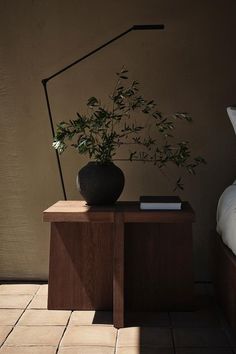 a plant sitting on top of a wooden table next to a bed