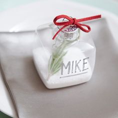 a white plate topped with a small glass vase filled with flowers next to a napkin