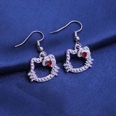 pair of heart shaped earrings with red stones on blue fabric background, close up view