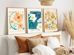 three framed art prints on the wall above a bed with white sheets and orange pillows