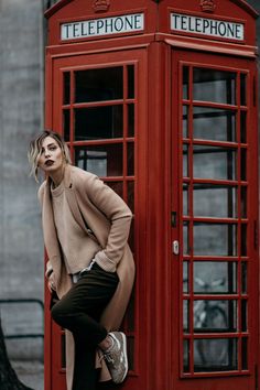 a woman leaning against a phone booth in front of a red telephone booth with her hands on her hips