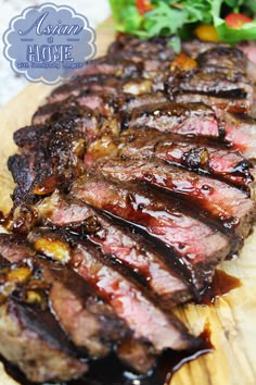 sliced steak on a wooden cutting board with sauce and salad in the backgroud