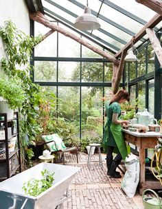 a woman standing in a greenhouse with lots of green plants and potted plants on the floor