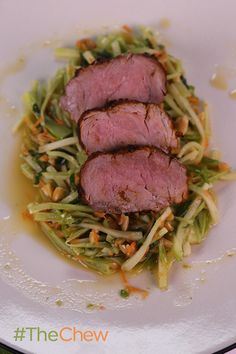 two slices of meat and noodles on a white plate with green sauce in the middle