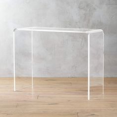 an acrylic table with clear legs in front of a concrete wall and wooden floor