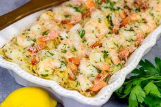 a casserole dish filled with shrimp and pasta next to lemons, parsley and parsley