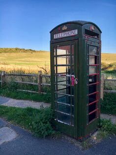 a green phone booth sitting on the side of a road next to a lush green field