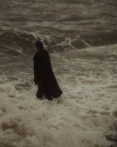 a man standing in the ocean with his back to the camera, looking out at the waves