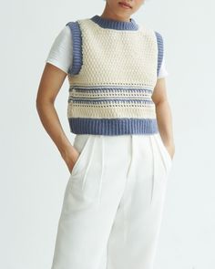 a woman standing in front of a white wall wearing a blue and white knitted sweater