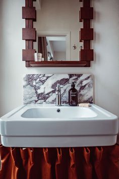 a white sink sitting under a mirror next to a wooden shelf with a bottle on it