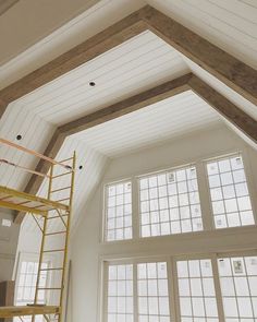 a ladder is in the middle of a room with large windows and wood beams on the ceiling