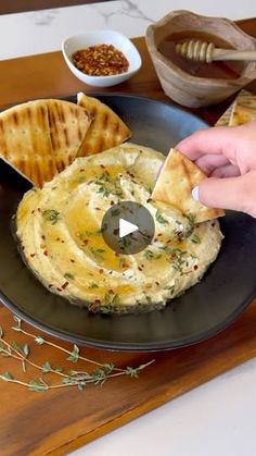 a person is holding a piece of bread over a plate with hummus and pita chips