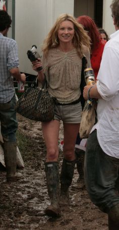 a woman in short shorts and boots walking down a dirt road with other people behind her