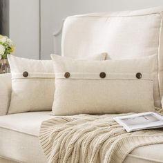 a white couch with two pillows and a magazine on the armrest next to it