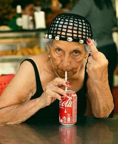 an old woman with a hat on her head drinking coca - cola