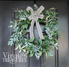 a wreath with a bow hanging on the front door is decorated with green leaves and greenery