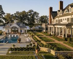 an outdoor swimming pool surrounded by lush green grass and shrubs next to a large white house