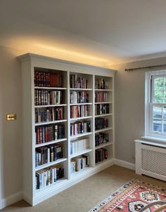 a living room filled with lots of books on top of a white book shelf next to a window