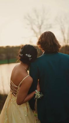 a man and woman in formal wear standing next to each other looking at the water