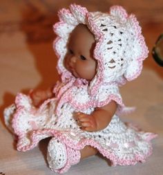 a baby doll wearing a crocheted dress and bonnet sitting on top of a table