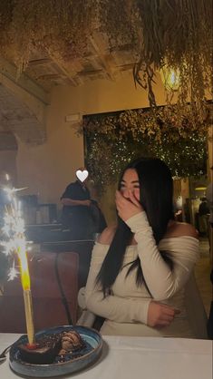 a woman sitting at a table in front of a cake with a lit candle on it