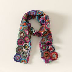 a multicolored crocheted scarf is displayed on a white surface with a shadow