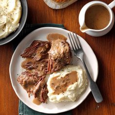 a plate with mashed potatoes, meat and gravy next to two mugs of coffee