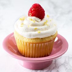 a cupcake with white frosting and a strawberry on top sits on a pink plate