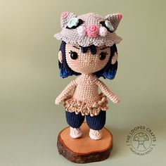 a crocheted doll is standing on top of a piece of wood and wearing a hat