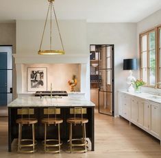 a large kitchen with an island and bar stools next to it, along with two windows