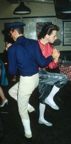 two men and a woman dancing together in an old fashioned dance studio, one man is holding the other's leg