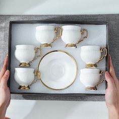 a person holding a tray with five white cups and saucers in it on top of a table