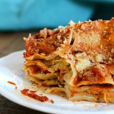 a white plate topped with lasagna covered in cheese and sauce on top of a wooden table