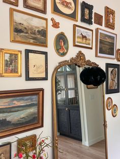 a wall full of paintings and pictures with a mirror on the wall next to it