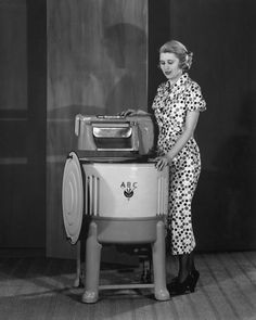 a woman standing next to an old fashioned washing machine