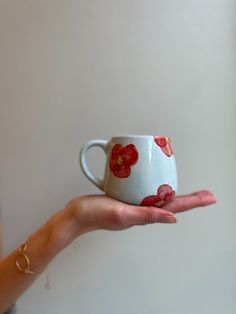 a hand holding a cup with red flowers on it