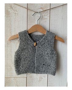 a gray knitted vest hanging on a wooden hanger next to a white wall