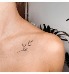 the back of a woman's shoulder with a small branch tattoo on her left shoulder