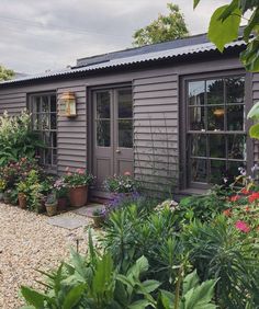 a small house with lots of plants and flowers around it