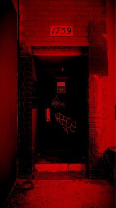 an open door with graffiti on it in front of a brick wall and red light