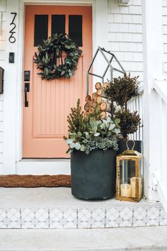 a potted plant next to a door with a wreath and lantern on the steps