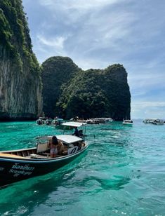 two boats are in the water near some rocks and cliffs, with people on them