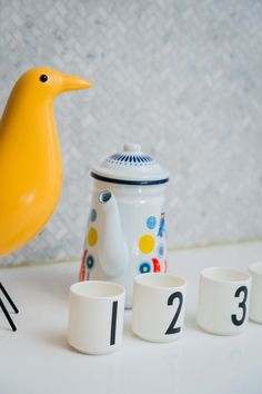 a yellow bird sitting on top of a table next to cups and mugs with numbers