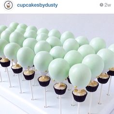 cupcakes with green frosting and white balloons on top are lined up in rows